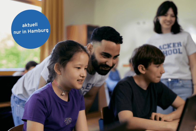 Zwei Schüler, ein Junge und ein Mädchen, arbeiten an Computern in einem Klassenzimmer. Zwei Inspirer der Hacker School schauen ihnen über die Schulter.