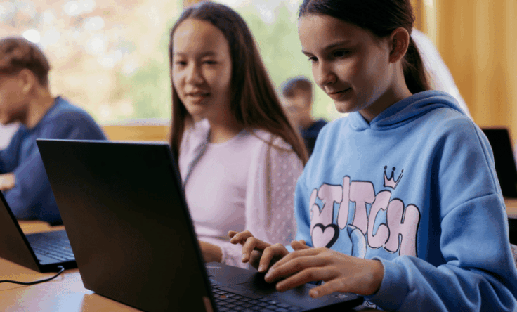 Zwei Schülerinnen arbeiten an Laptops in einem Klassenzimmer.